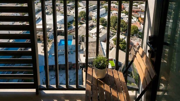 A balcony with a wooden chair and a potted plant, overlooking a cityscape with mountains in the distance. - Maravilloso Apt 7px Frente arena Mty (Monterrey)