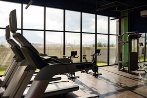 A gym with exercise equipment, large windows, and a view of a cityscape.