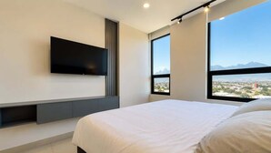 Una habitación de hotel moderna con una cama grande, un televisor montado y vistas a la ciudad.