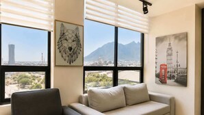 Una sala de estar con sofá, una silla, una ventana con persianas y obras de arte en las paredes.