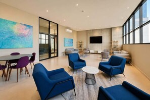 A modern lounge with blue armchairs, a round coffee table, and a large abstract painting on the wall.