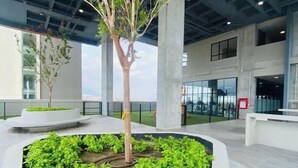 A modern indoor space with a central planter containing a tree and green plants, surrounded by concrete pillars and a glass wall. - Fundidora Loft w/Parking & AC, Near Arena (Monterrey)