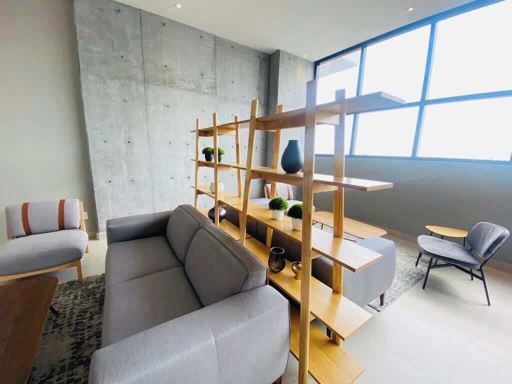 A modern living room with a grey sofa, wooden shelves, and a dining area.