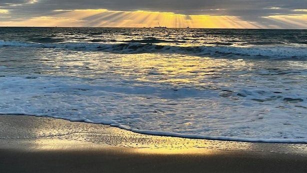 Una playa con olas, cielo nublado y luz solar.