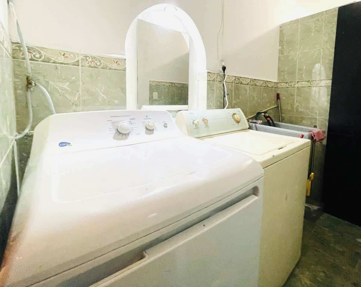 A laundry area with a washing machine and dryer, a mirror, and tiled walls.