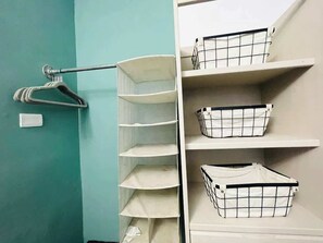 Un armario con estantes blancos y espacio para colgar, que incluye un perchero de metal y cestas.