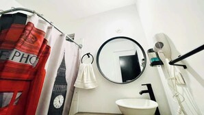 A bathroom with a white sink, a round mirror, a hairdryer, and a shower curtain with a clock design. - Comodo Loft/Ac/Tv/Wifi/2px (Monterrey)