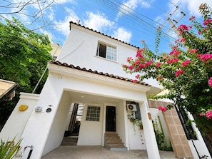 A two-story white building with a tiled roof, a front entrance with a staircase, and a small window. - Monterrey Gem: Garden, Modern Comforts, Fast WiFi (Monterrey)