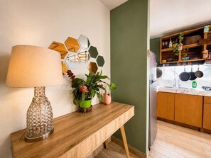 Ein Holzkonsolentisch mit Lampe, Topfpflanzen und sechseckiger Wanddeko in einer modernen Küche mit Holzschränken und einer grünen Akzentwand.