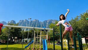 Ein Spielplatz mit Rutsche, Klettergerüsten und einem Kind, das an einem Reck geht.
