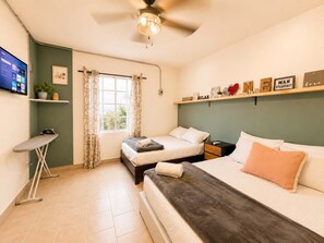 Une chambre avec deux lits, un bureau, un ventilateur de plafond, une fenêtre avec des rideaux et une étagère contenant des objets inspirants.