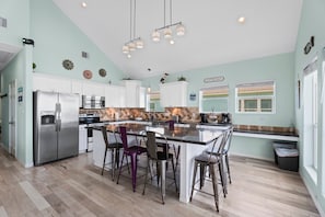 A kitchen with white cabinets, a stainless steel refrigerator, a coffee bar, and a large island with bar stools. - Beachfront with Hot Tub & Putt Putt | Sleeps 16 (Gilchrist)