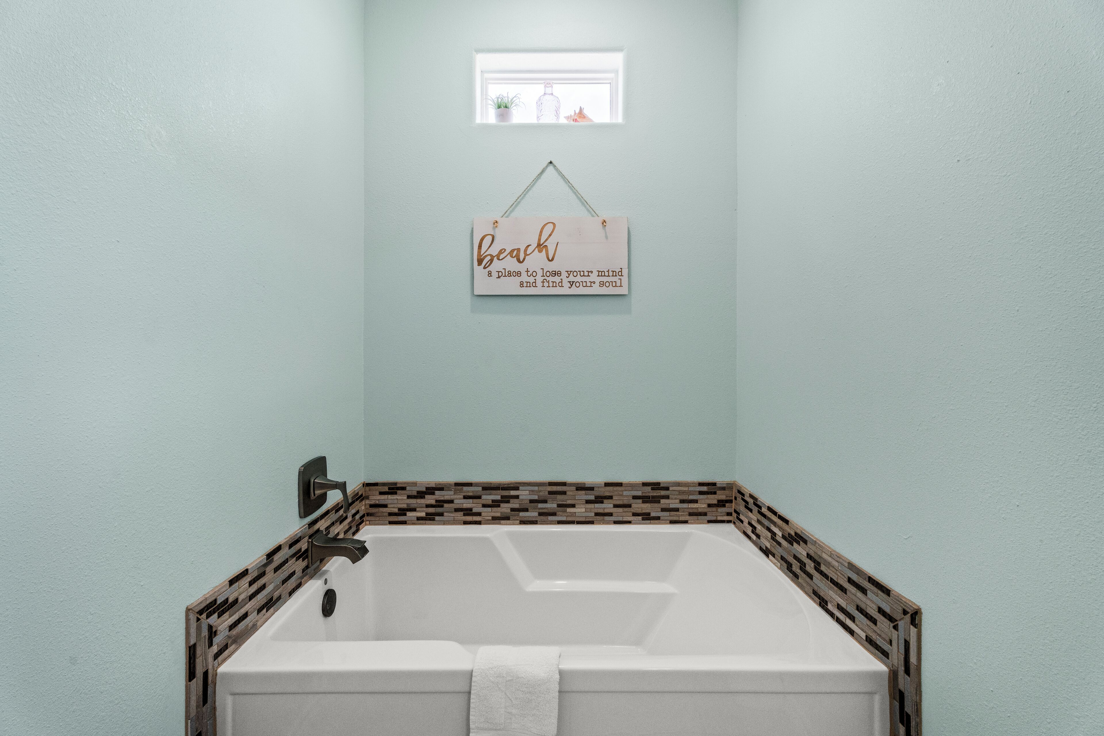 Une salle de bain avec une baignoire, une petite fenêtre ornée de plantes et un panneau accroché au mur.
