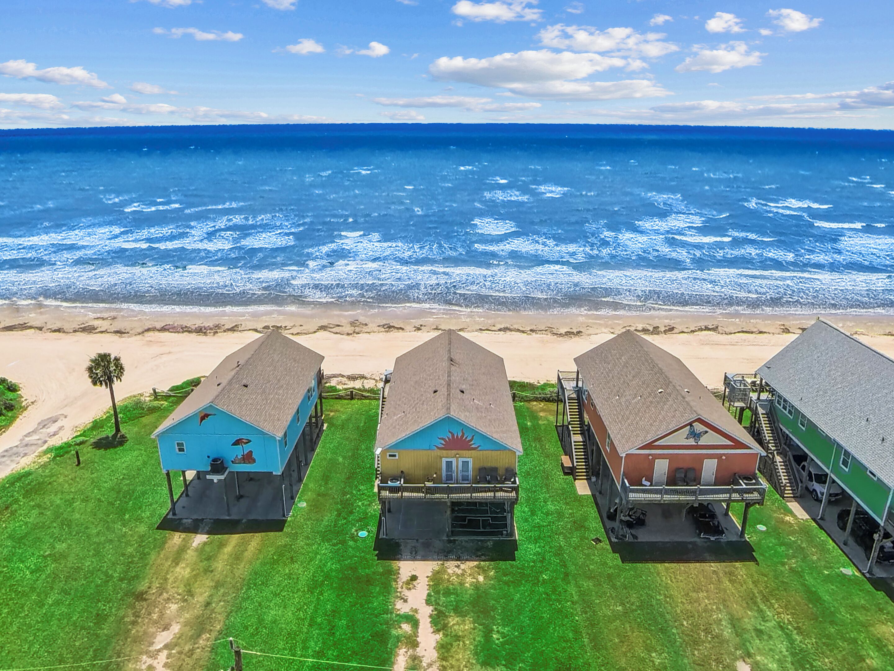 A beachfront property with three houses, a sandy beach, and the ocean in the background.