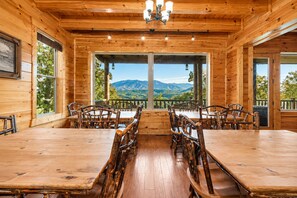 Ein Holzinnenraum mit Esstisch und Stühlen, großen Fenstern mit Bergblick und einer Chandelier.