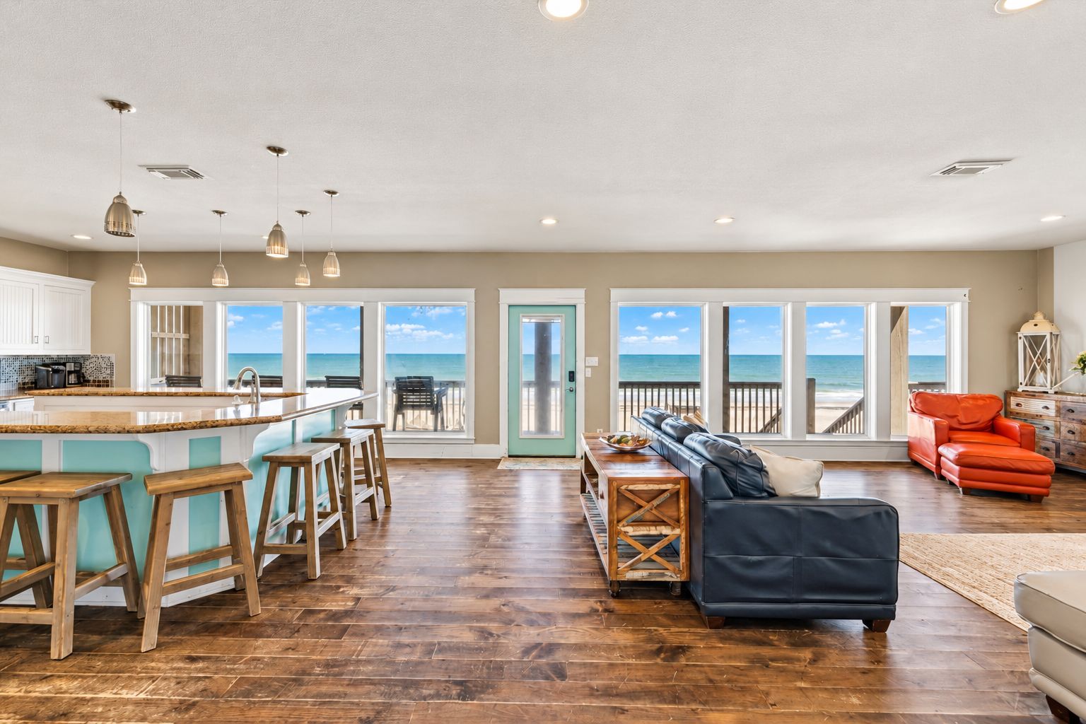 A spacious living area with a large window overlooking the beach, a kitchen with a bar area, and a cozy seating arrangement.