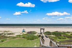 Blick auf einen Strand mit einer Holzpromenade, die zu einem Gazebo führt.