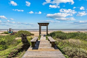 Ein Holzsteg führt zu einem Strandpavillon mit Bänken.