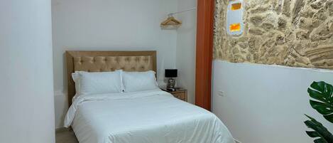 A bedroom with a bed, a nightstand, a wall-mounted air conditioner, and a stone wall with a small window.