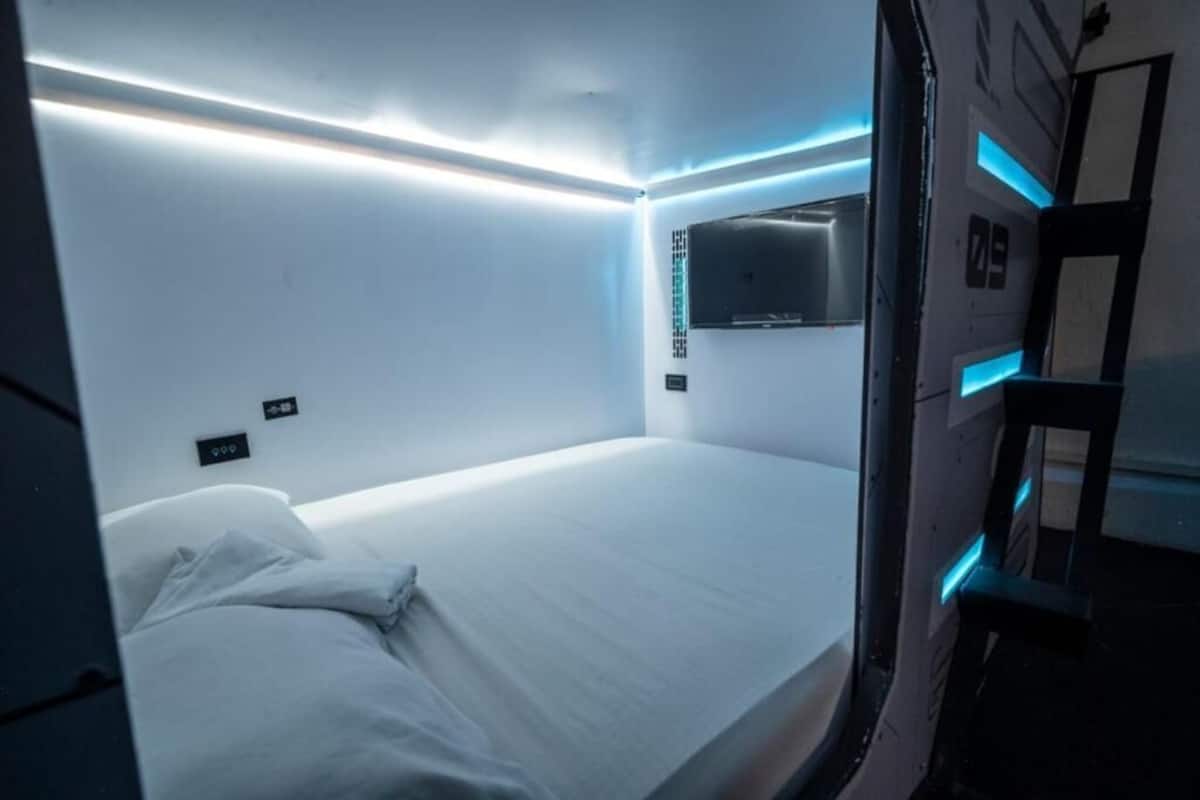 A modern hotel room with a neatly made bed, a flat-screen TV mounted on the wall, and ambient lighting.