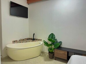 A bathroom with a bathtub, a sink, a mirror, a potted plant, and a flat-screen TV mounted on the wall. - Hotel Victoria Caps (Cartagena)