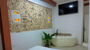 Ein Zimmer mit Bett, Wand-Fernseher, Badewanne und einer Topfpflanze.