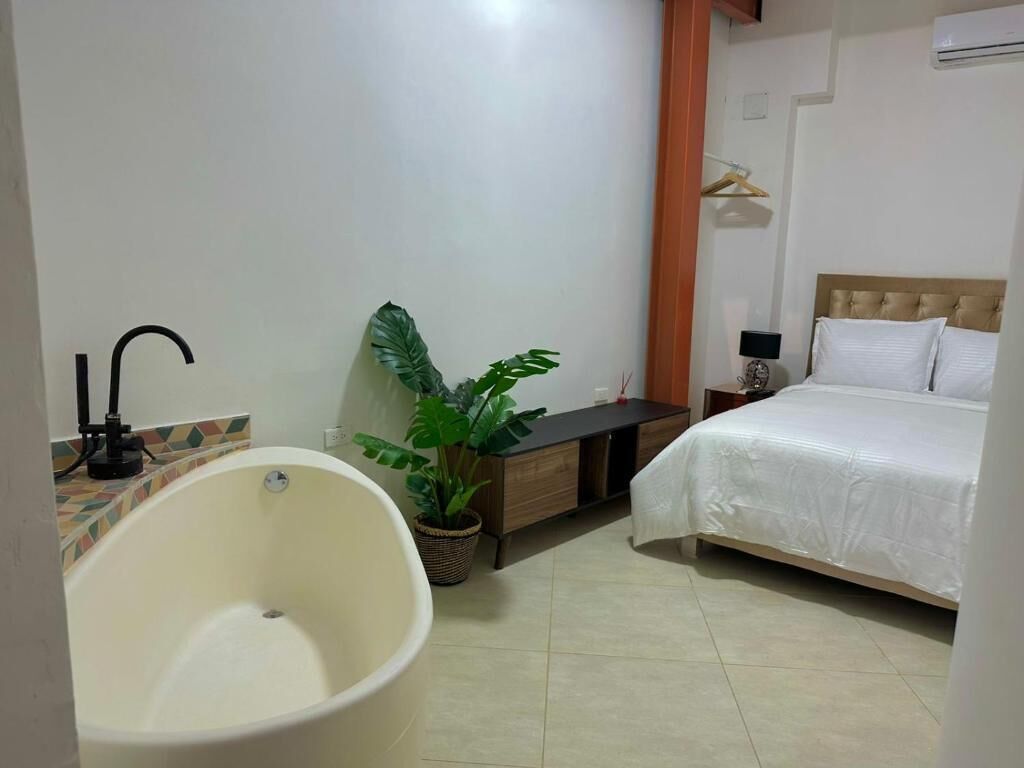 Un baño con bañera, lavamanos, planta en maceta y mesita de noche con lámpara.