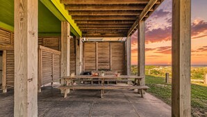 An outdoor wooden structure with a picnic table, benches, and a view of the beach at sunset. - Beachfront 5BR | Gulf Views + Game Room with Pool Table (Port Bolivar)