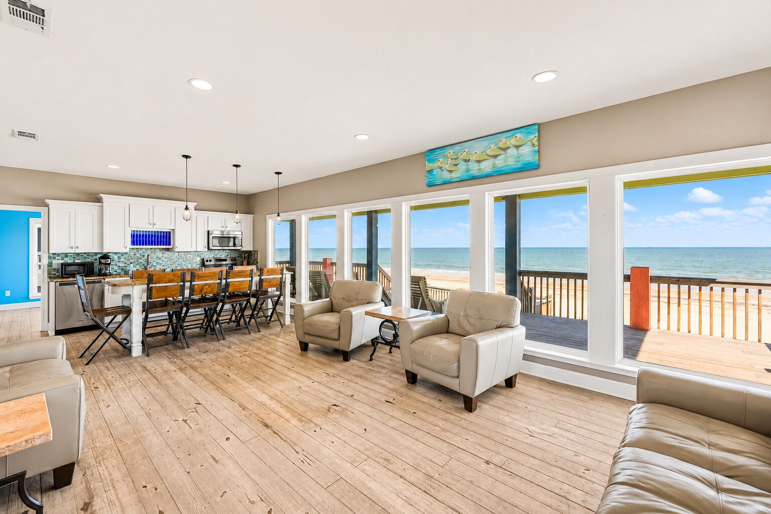 A spacious living area with a wooden floor, a dining set, and a view of the beach.