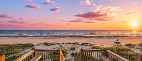 A wooden boardwalk leading to a beach with a sunset in the background.