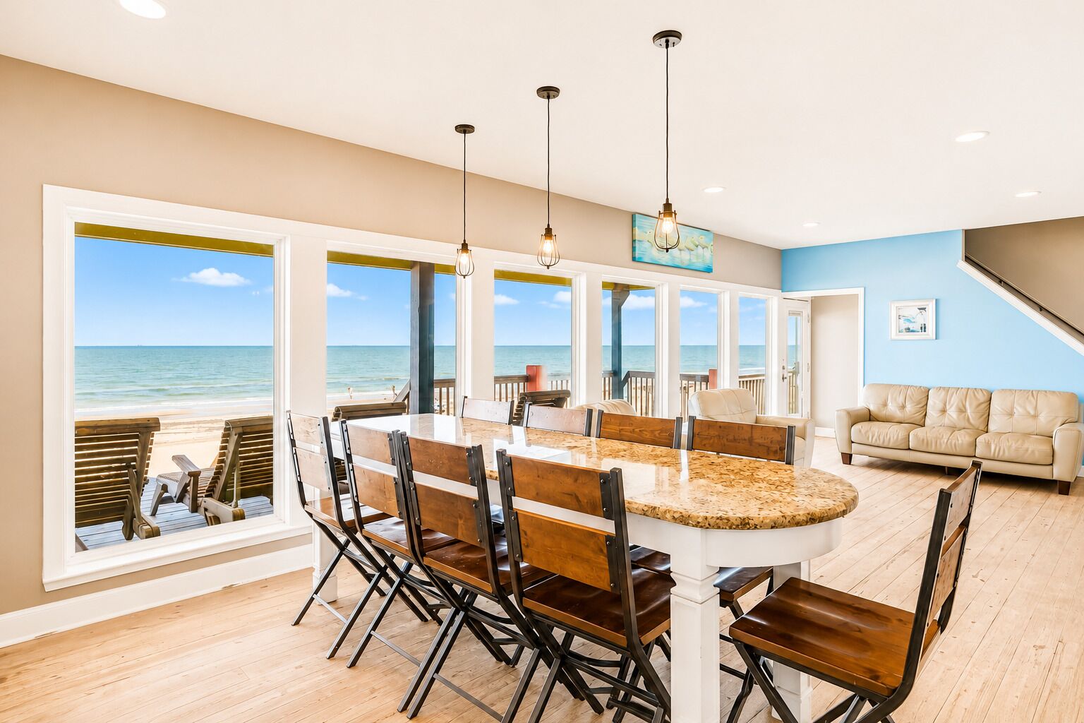 A spacious dining area with a view of the ocean, a large round table, and modern pendant lighting.
