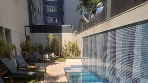 Una piscina con pared de azulejos, sillas de descanso y solárium de hormigón.
