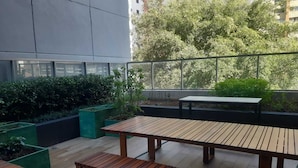 Un patio al aire libre con una mesa y bancos de madera, rodeado de follaje y vistas a árboles.