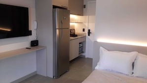 Habitación de hotel compacta con cama, kitchenette pequeña, refrigerador, televisor de pantalla plana y teléfono junto a la cama.