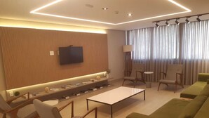 Una sala de estar moderna con una televisión de pantalla plana, un sofá, sillas, una mesa de centro y una estantería.