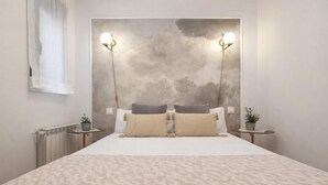 Una camera da letto con un letto grande, due comodini, un punto luce a parete e una finestra con tende leggere.
