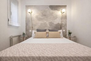 A bedroom with a large bed, two bedside tables, a wall-mounted light fixture, and a window with sheer curtains. - Gran Vía VI (Madrid)