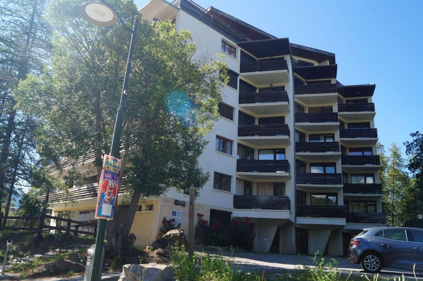 A multi-story residential building with balconies, a street lamp, and a parked car.