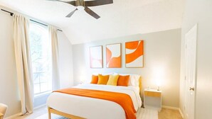 Une chambre à coucher avec un lit, un ventilateur de plafond, une table de chevet et une fenêtre avec des rideaux.