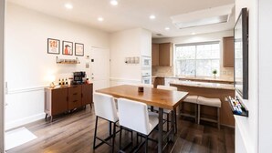 Une cuisine moderne avec une table en bois et des chaises blanches, un coin bar et une grande fenêtre.