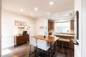 A modern kitchen with a wooden table and white chairs, a bar area, and a large window. - Stay at Golden Hour | Pool + Hot Tub | Sleeps 10+ (Irving)