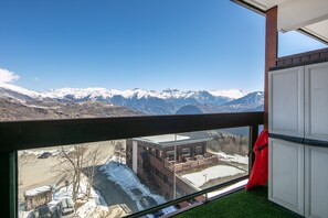 Ein Zimmer mit Blick auf schneebedeckte Berge, ein Balkon mit einem roten Stuhl und ein Gebäude mit einer Ziegel-Fassade.