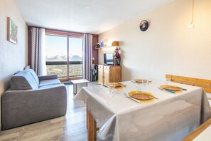 Ein Zimmer mit einer Couch, einem Esstisch für zwei Personen, einem Fernseher und Blick auf die Berge.