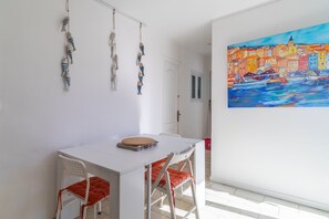 Ein Zimmer mit einem weißen Tisch, zwei Stühlen, einem Bild einer Küstenstadt und hängenden Spielzeugfischen.