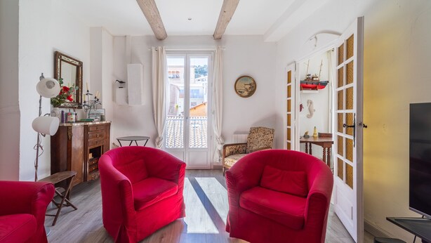 Una habitación con dos sillas rojas, un escritorio de madera con una lámpara, un espejo y vistas por una puerta.