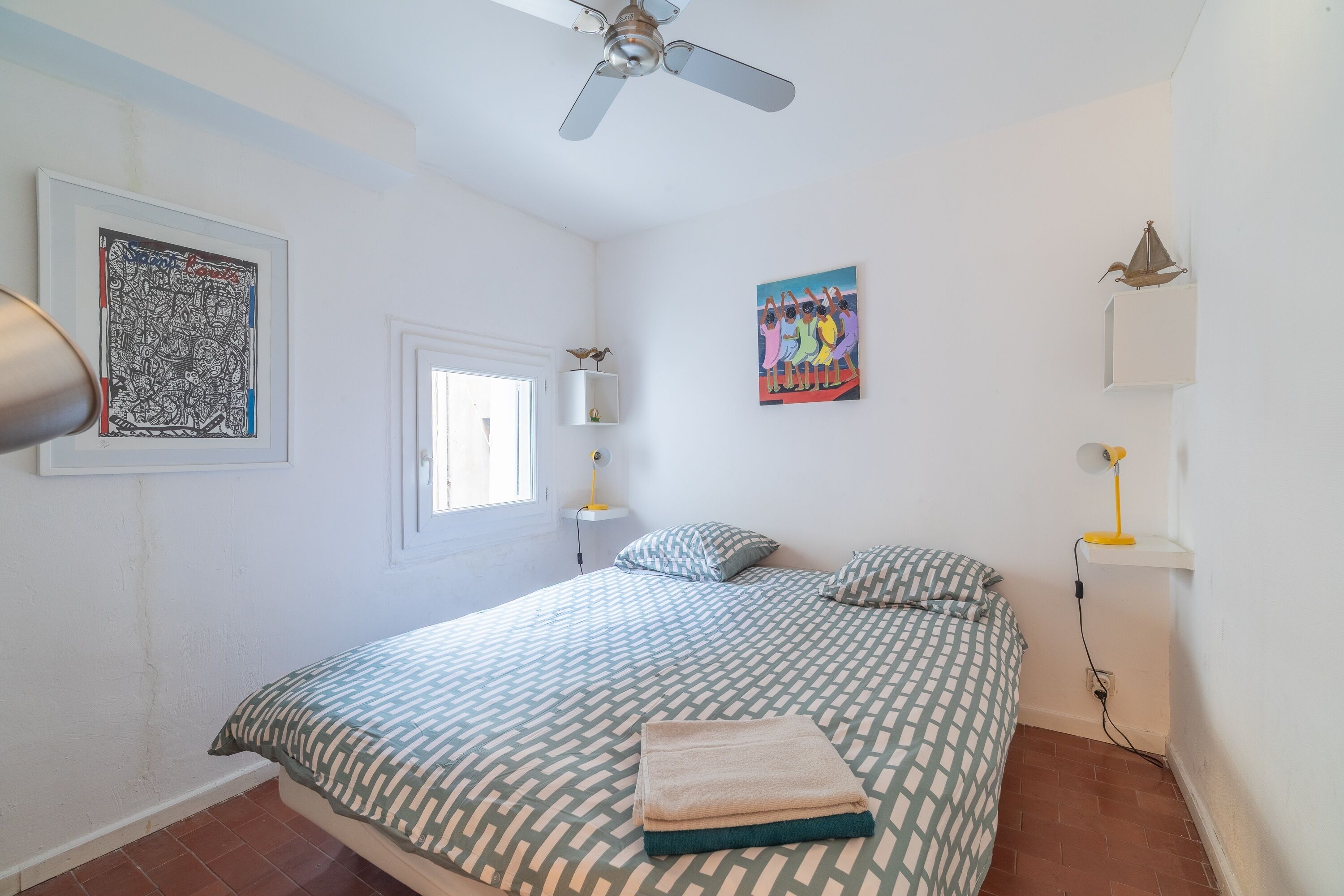 Une chambre à coucher avec un lit, un ventilateur de plafond, des œuvres d’art et une fenêtre.