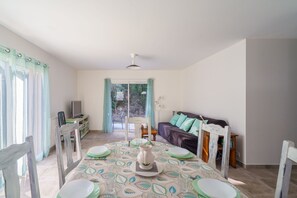 A dining area with a table set for four, a sofa, and a television in the background. - Le Refuge de la Fontaine - Maison 25min de Quimper (Saint-Coulitz)