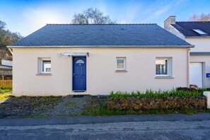 A single-story house with a blue door, a small window on each side, and a stone wall in front. - Le Refuge de la Fontaine - Maison 25min de Quimper (Saint-Coulitz)