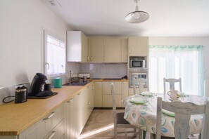 A kitchen with a microwave, coffee maker, and a dining table set for two. - Le Refuge de la Fontaine - Maison 25min de Quimper (Saint-Coulitz)