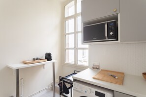 A compact kitchen with a microwave, a washing machine, and a drying rack.